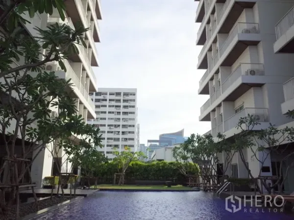 公寓 出租在Watthana, Bangkok - 公寓庭院泳池，位于两栋现代建筑之间并环绕绿化。