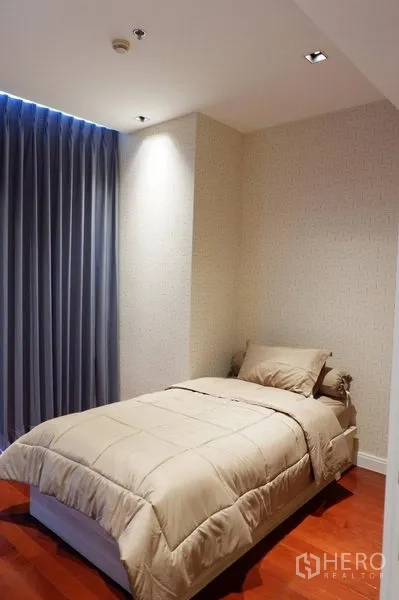 คอนโด ให้เช่าในPathum Wan, Bangkok - ห้องนอนที่สองขนาดกะทัดรัด เตียงเดี่ยว ผ้าม่านทึบสีน้ำเงิน และพื้นไม้