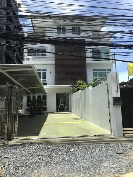 带办公室的家 出租或出售在Watthana, Bangkok - 现代四层家用办公楼外观，带大门庭院、遮阳车位与多处阳台。