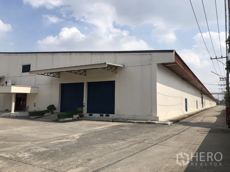 货栈 出租在Lam Luk Ka, Pathum Thani - 仓库转角立面，雨棚覆盖的双装卸门及车道入口
