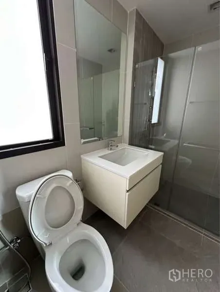 Townhouse for rent in Lat Phrao, Bangkok - Bright bathroom with vanity, toilet and a glass-enclosed shower beside a window.