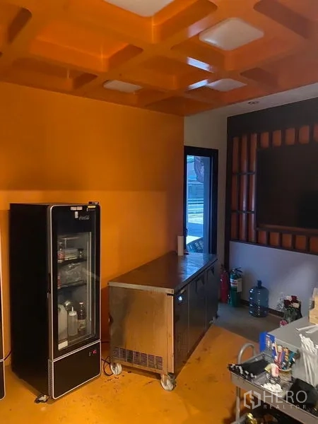 Shophouse for rent - Service room with orange ceiling, glass-door fridge, and stainless steel workstation.