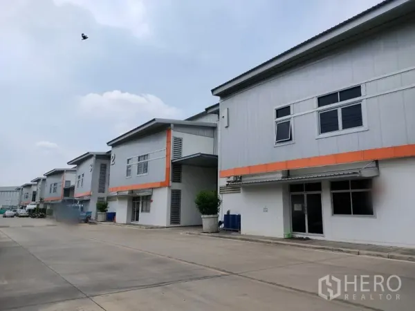 Factory for rent in Phra Nakhon Si Ayutthaya - Row of modern factory units with orange trim and a wide driveway in an industrial estate.