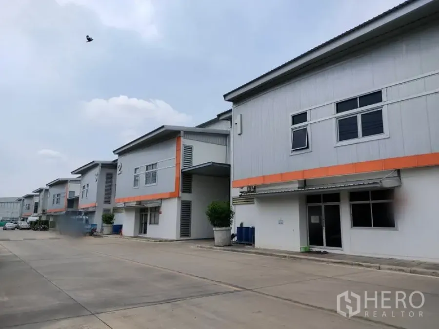 Factory for rent in Phra Nakhon Si Ayutthaya - Row of modern factory units with orange trim and a wide driveway in an industrial estate.