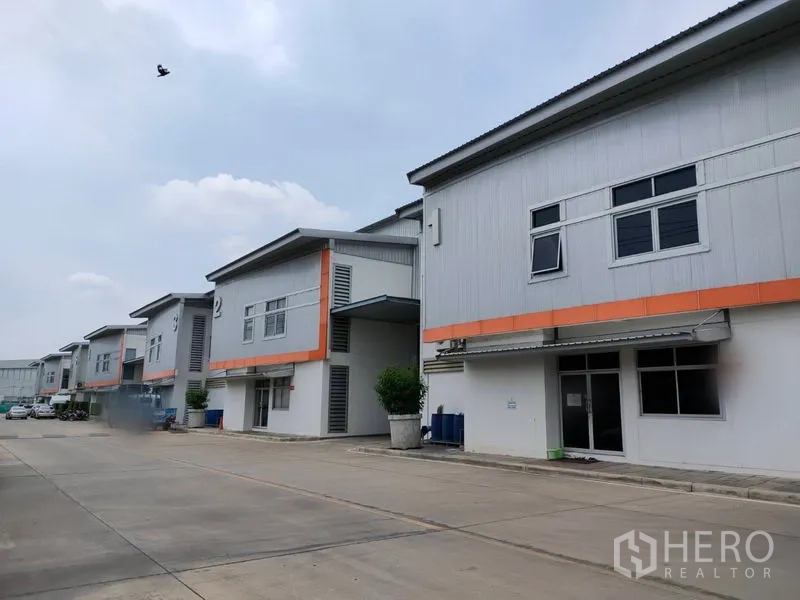 Factory for rent in Phra Nakhon Si Ayutthaya - Row of modern factory units with orange trim and a wide driveway in an industrial estate.
