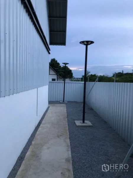 Warehouse for rent in Bueng Kum, Bangkok - Side gravel walkway beside the warehouse with perimeter fencing and pole lights