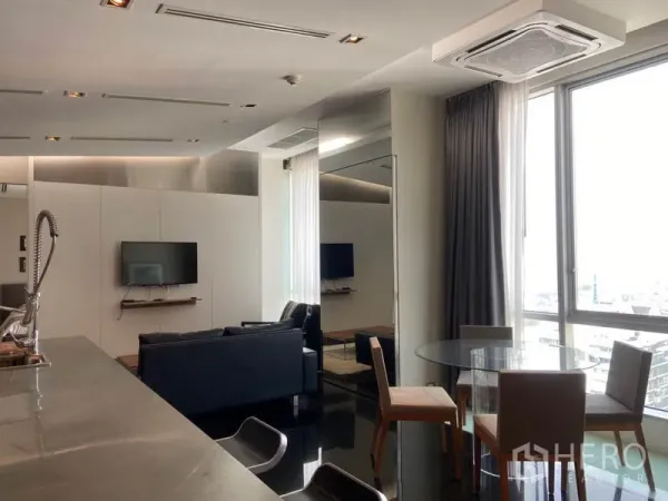 Condominium for rent in Sathon, Bangkok - Dining corner with a round glass table beside a large window, adjoining the kitchen and living area.