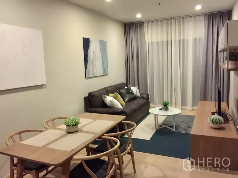 Condominium for rent in Bangkok - Cozy lounge with leather sofa, wall art, round coffee table and sheer blackout drapes in a contemporary condominium.