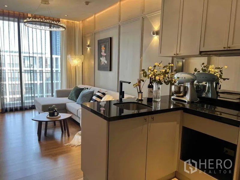 Condominium for rent or sale in Watthana, Bangkok - Open-plan living with peninsula kitchen, chandelier and large windows to balcony.