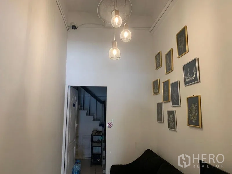 Shophouse for rent in Khlong Toei, Bangkok - Compact lounge with pendant lights, framed artwork, and a view toward the staircase.