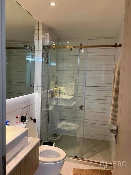 Condominium for sale in Huai Khwang, Bangkok - Contemporary bathroom featuring a glass-enclosed shower, white wall tiles and a sleek vanity with vessel sink.