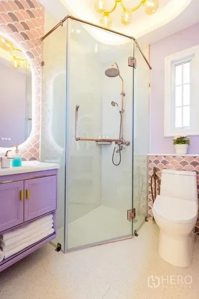 Townhouse for rent in Lat Phrao, Bangkok - Bathroom featuring a glass corner shower, lavender vanity, round mirror and soft pastel tiles.