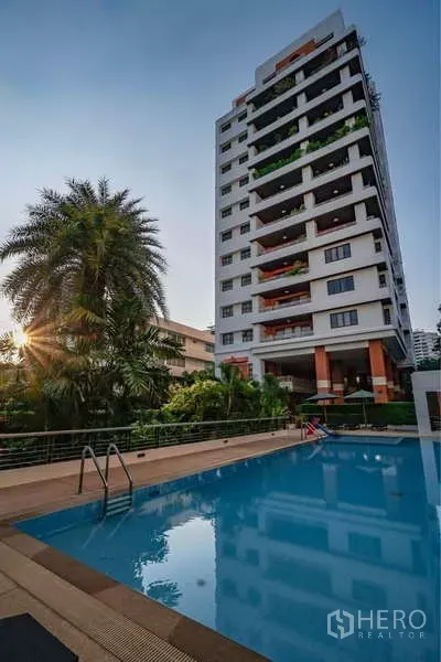 Apartment for rent in Sathon, Bangkok - Mid-rise residential tower at Baan Suan Chan with outdoor swimming pool and landscaped garden at sunset.