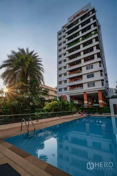 Apartment for rent in Sathon, Bangkok - Mid-rise residential tower at Baan Suan Chan with outdoor swimming pool and landscaped garden at sunset.