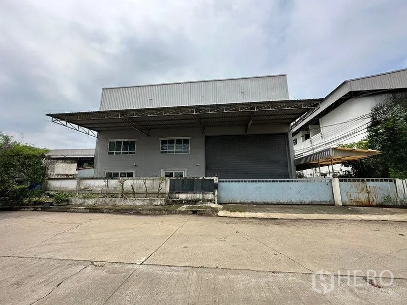 Factory for rent or sale in Bang Bua Thong, Nonthaburi - Modern factory exterior in Bang Bua Thong with wide driveway, high canopy roof and large roller shutter gate.