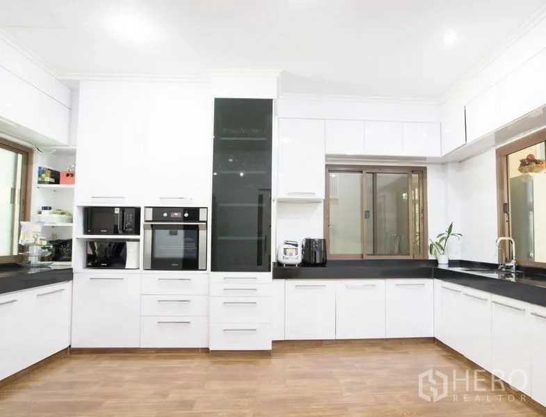 Detached House for sale in Lat Krabang, Bangkok - Modern white U-shaped kitchen with stone countertops, built-in oven and microwave, and large windows.