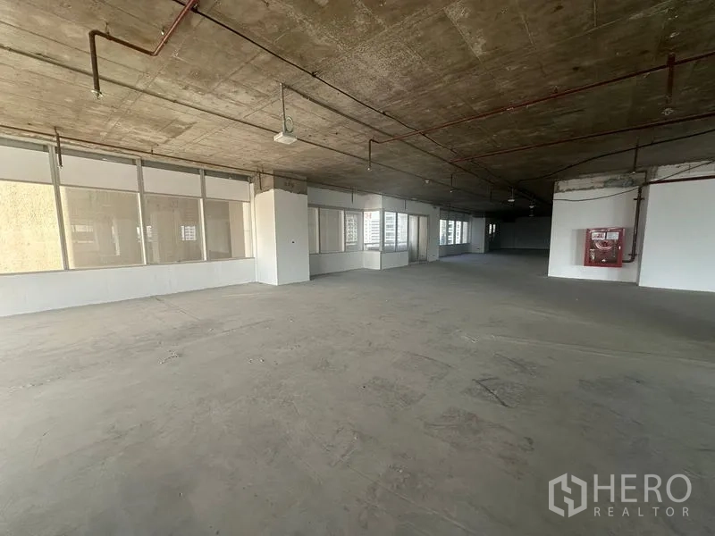 Office Space for rent in Watthana, Bangkok - Large open-plan office floor with exposed concrete ceiling, perimeter windows, and a wall-mounted fire hose cabinet.