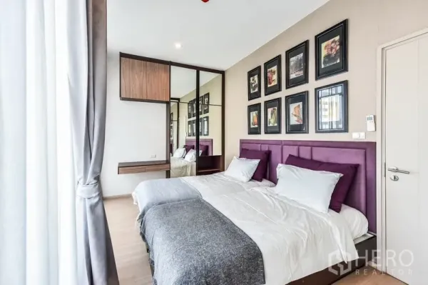 Condominium for rent or sale in Huai Khwang, Bangkok - Bedroom with twin beds, framed artwork, mirrored wardrobe, and soft curtains.