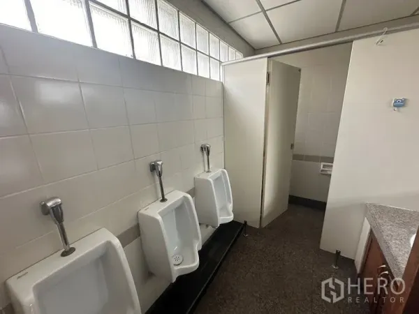 办公空间 出租 - 办公楼男厕，三个挂墙式小便斗，瓷砖墙面，隔间与玻璃砖采光窗。