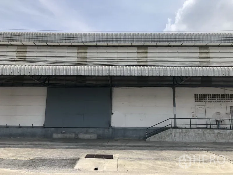 货栈 出租在Khlong Luang, Pathum Thani - 仓库外立面，带长雨棚的抬高装卸平台和大型滑动门，卡车进出便捷。