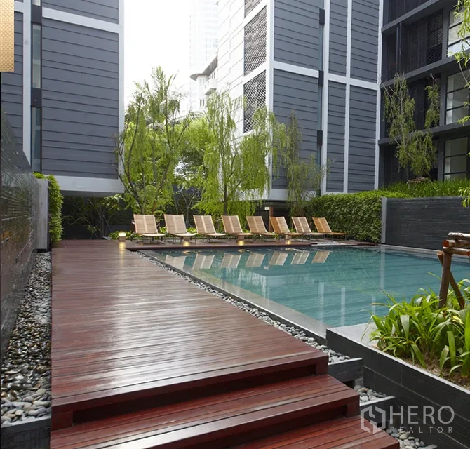 公寓 出租在Watthana, Bangkok - 公寓户外泳池配木质甲板、躺椅与绿化景观。