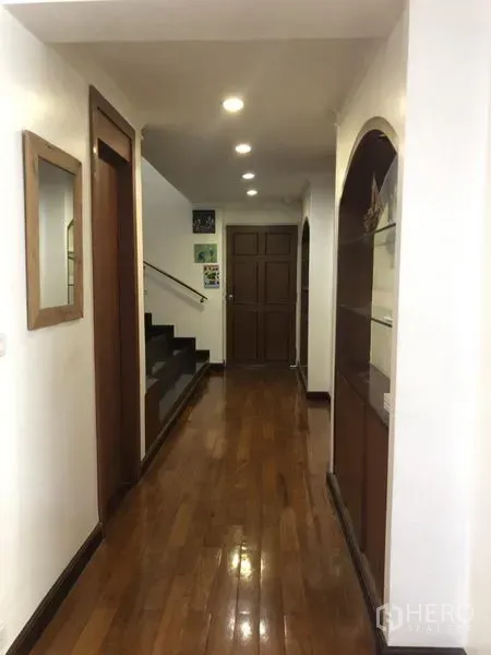 Condominium for sale in Watthana, Bangkok - Well-lit hallway with recessed ceiling lights and a wooden staircase.