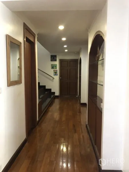 Condominium for sale in Watthana, Bangkok - Well-lit hallway with recessed ceiling lights and a wooden staircase.