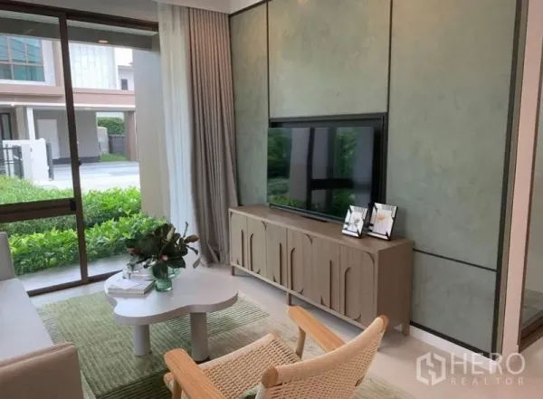 Detached House for sale in Bang Kapi, Bangkok - Cozy TV lounge with feature wall, media console and floor-to-ceiling windows overlooking greenery.
