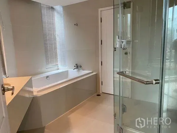 Condominium for rent in Pathum Wan, Bangkok - Modern bathroom featuring a built-in bathtub, glass-enclosed shower and daylight window.