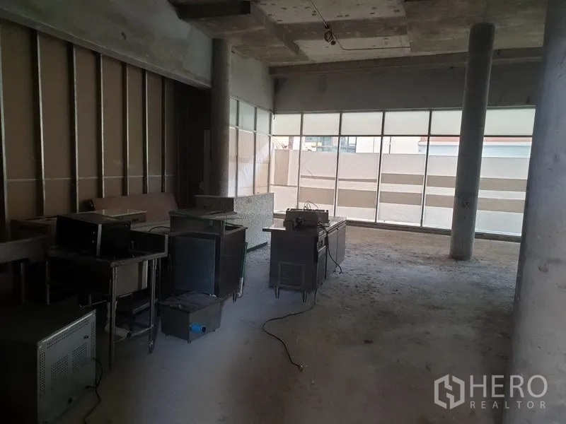 零售空间 出租在Khlong Toei, Bangkok - 未装修的零售铺位，混凝土天花与立柱，正面大窗，地面有设备摆放。