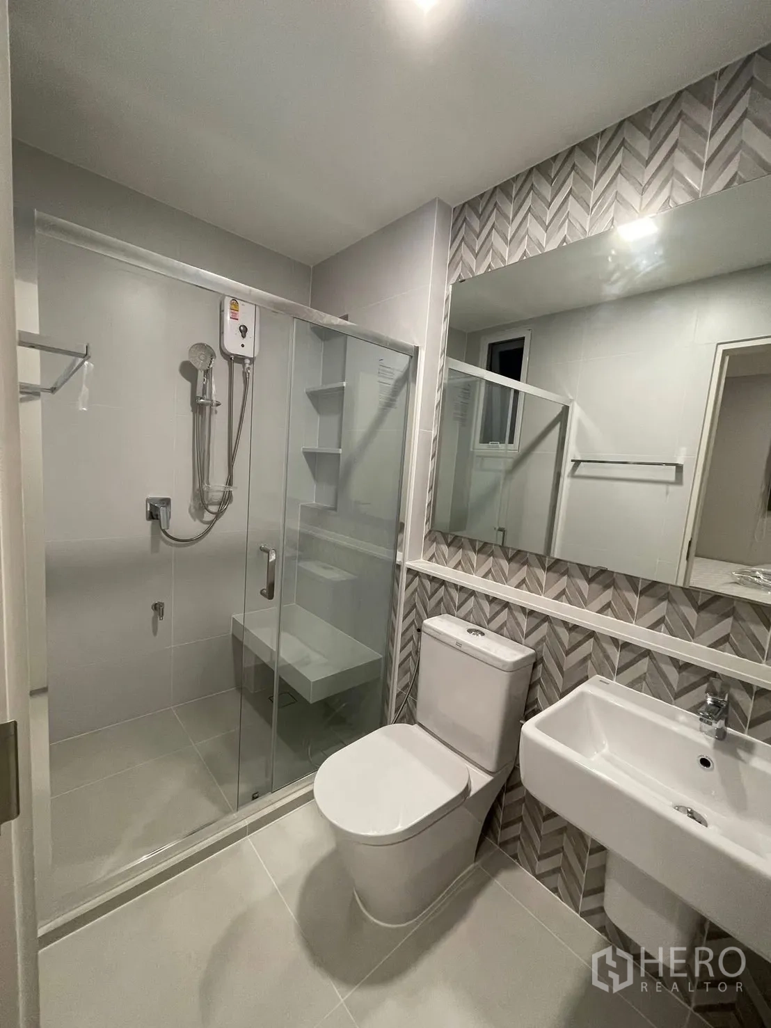 独栋房屋 for rent in Prawet, Bangkok - 浴室带人字纹装饰墙、玻璃淋浴房与白色洁具。