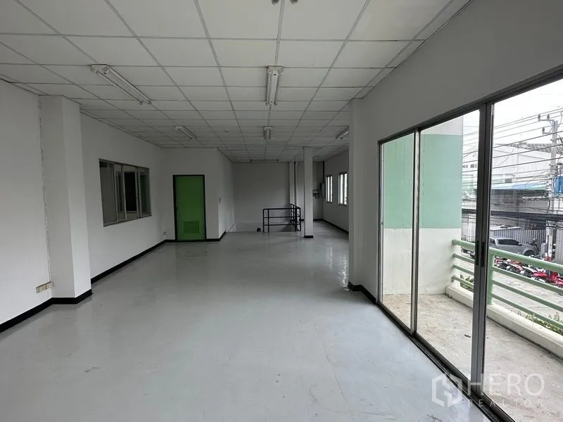 Factory for rent in Khlong Luang, Pathum Thani - Upper-floor office corridor with large sliding glass doors opening to a balcony over the parking area.