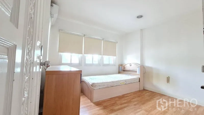 独立式住宅 出租在Lat Phrao, Bangkok - 温馨卧室，木纹地板，床与矮柜，三扇带百叶的窗。