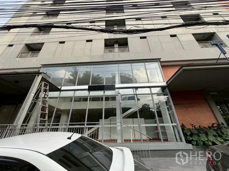 Retail Space for rent in Watthana, Bangkok - Ground-floor glass storefront of a modern mixed-use building with entry steps and parking.