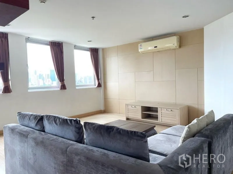 Condominium for rent in Khlong Toei, Bangkok - Lounge with large windows, city views, wall-mounted air conditioner and low TV console.