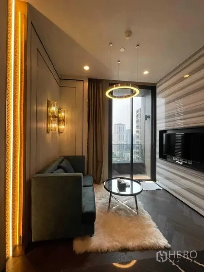 Condominium for rent in Khlong Toei, Bangkok - Compact living space with sofa, round glass coffee table, ring pendant and balcony view.