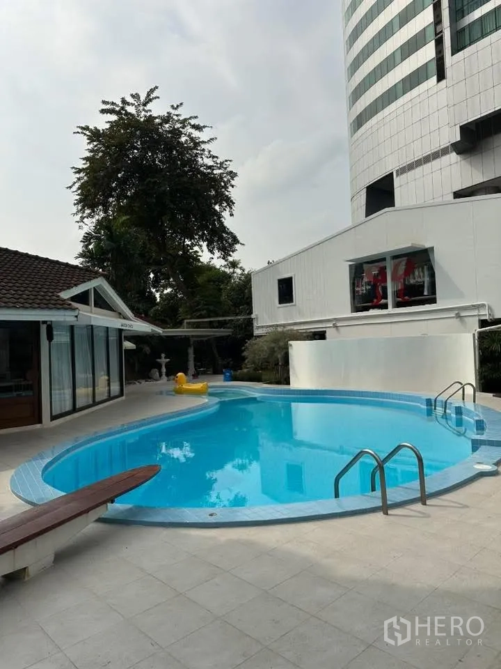 Retail Space for rent in Khlong Toei, Bangkok - Curved swimming pool with stainless steps and tiled deck beside low-rise buildings.