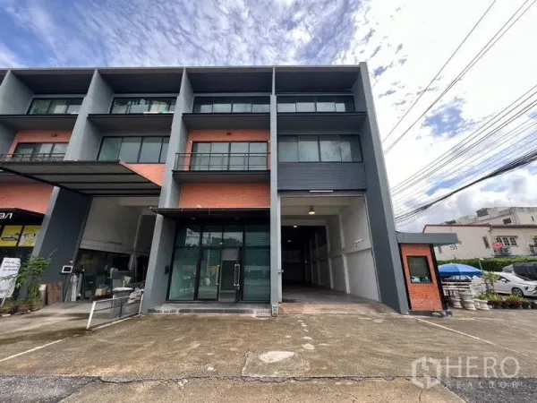 货栈 出租在Bang Phli, Samut Prakan - 三层仓库外立面，红砖点缀，玻璃办公室、装卸通道与停车区。