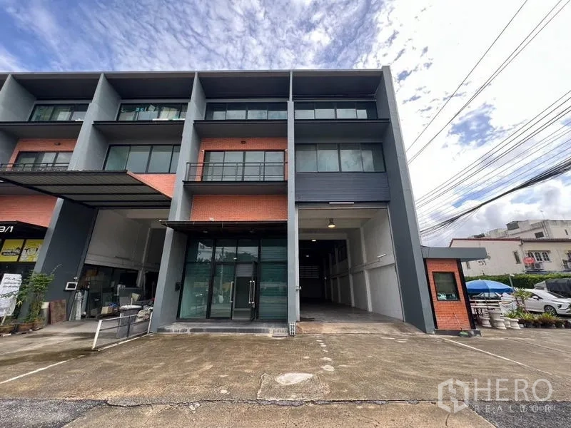 货栈 出租在Bang Phli, Samut Prakan - 三层仓库外立面，红砖点缀，玻璃办公室、装卸通道与停车区。