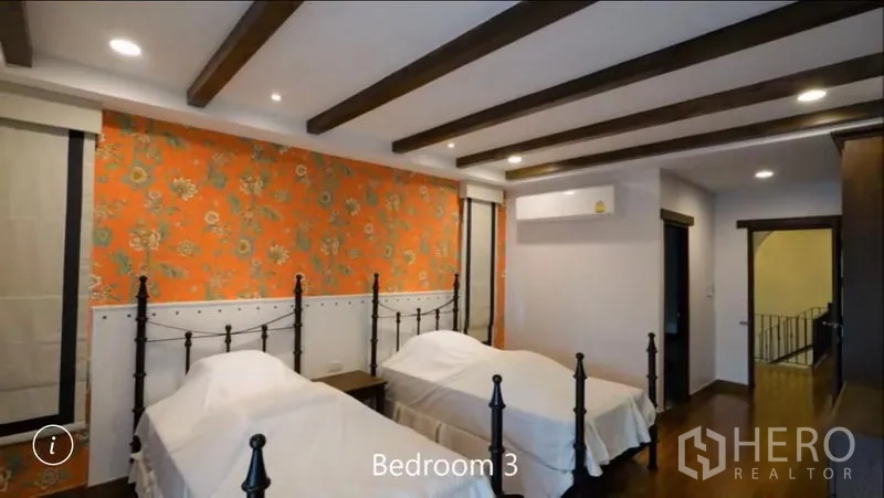 Detached House for rent or sale in Bang Phli, Samut Prakan - Twin-bed bedroom with exposed ceiling beams, floral orange accent wall and wood flooring.
