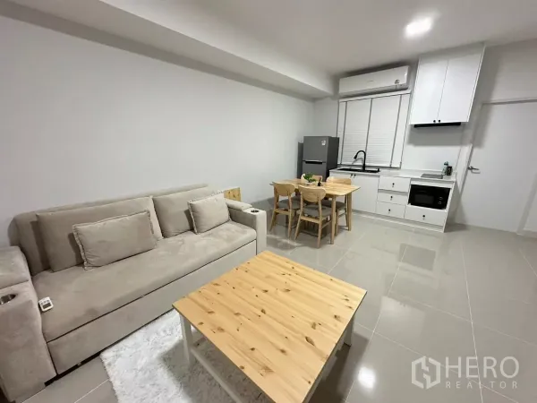 Townhouse for rent in Bang Phli, Samut Prakan - Open‑plan living and dining area with sofa, four‑seat table and a white built‑in kitchen.
