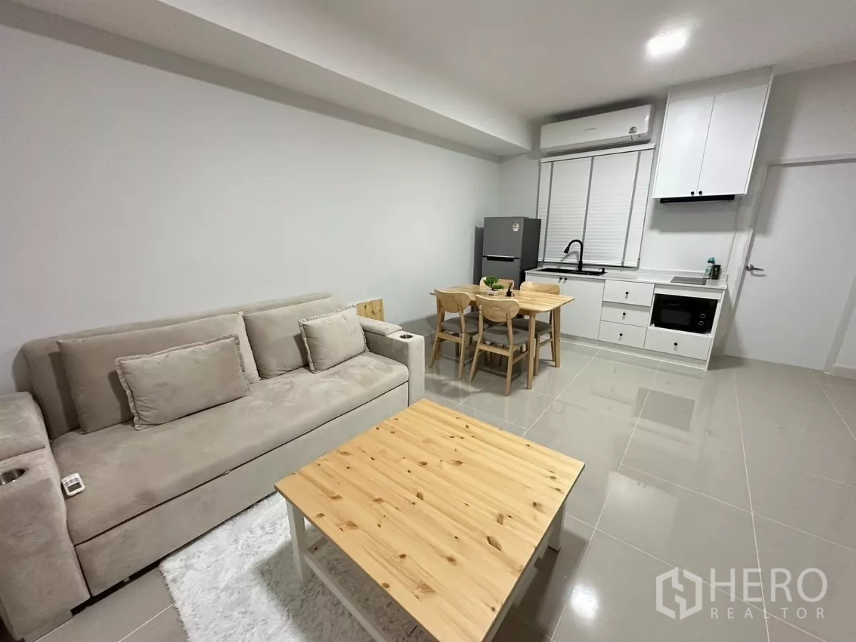 Townhouse for rent in Bang Phli, Samut Prakan - Open‑plan living and dining area with sofa, four‑seat table and a white built‑in kitchen.