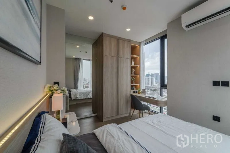 Condominium for rent in Pathum Wan, Bangkok - Compact bedroom featuring wardrobe, corner study desk and tall windows with city views.
