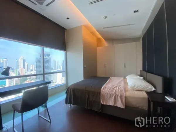 Condominium for rent in Sathon, Bangkok - Bedroom with desk by a panoramic window overlooking the Sathorn skyline and built-in wardrobes.
