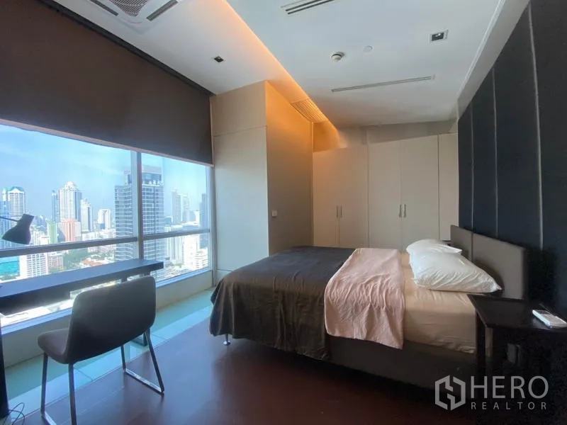 Condominium for rent in Sathon, Bangkok - Bedroom with desk by a panoramic window overlooking the Sathorn skyline and built-in wardrobes.