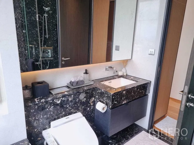 Condominium for sale - Modern bathroom with black marble vanity, large mirror and glass-enclosed shower.