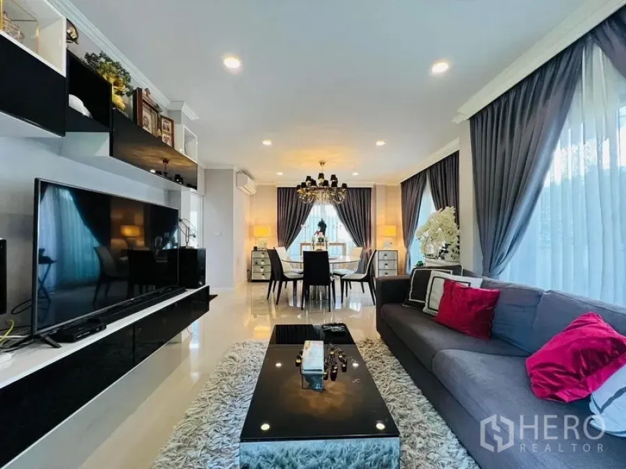 Detached House for rent or sale in Bang Khen, Bangkok - Open-plan living and dining room with chandelier, grey curtains, large TV and glossy tile floor.