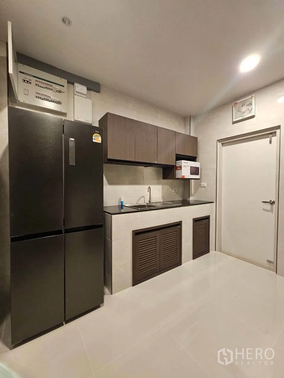 Detached House for rent or sale in Bang Phli, Samut Prakan - Kitchen view with double-door refrigerator, sink, and overhead cupboards.