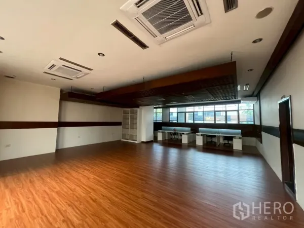 Retail Space for rent - Spacious retail hall with wood flooring, suspended ceiling beams, shelving and wide windows.