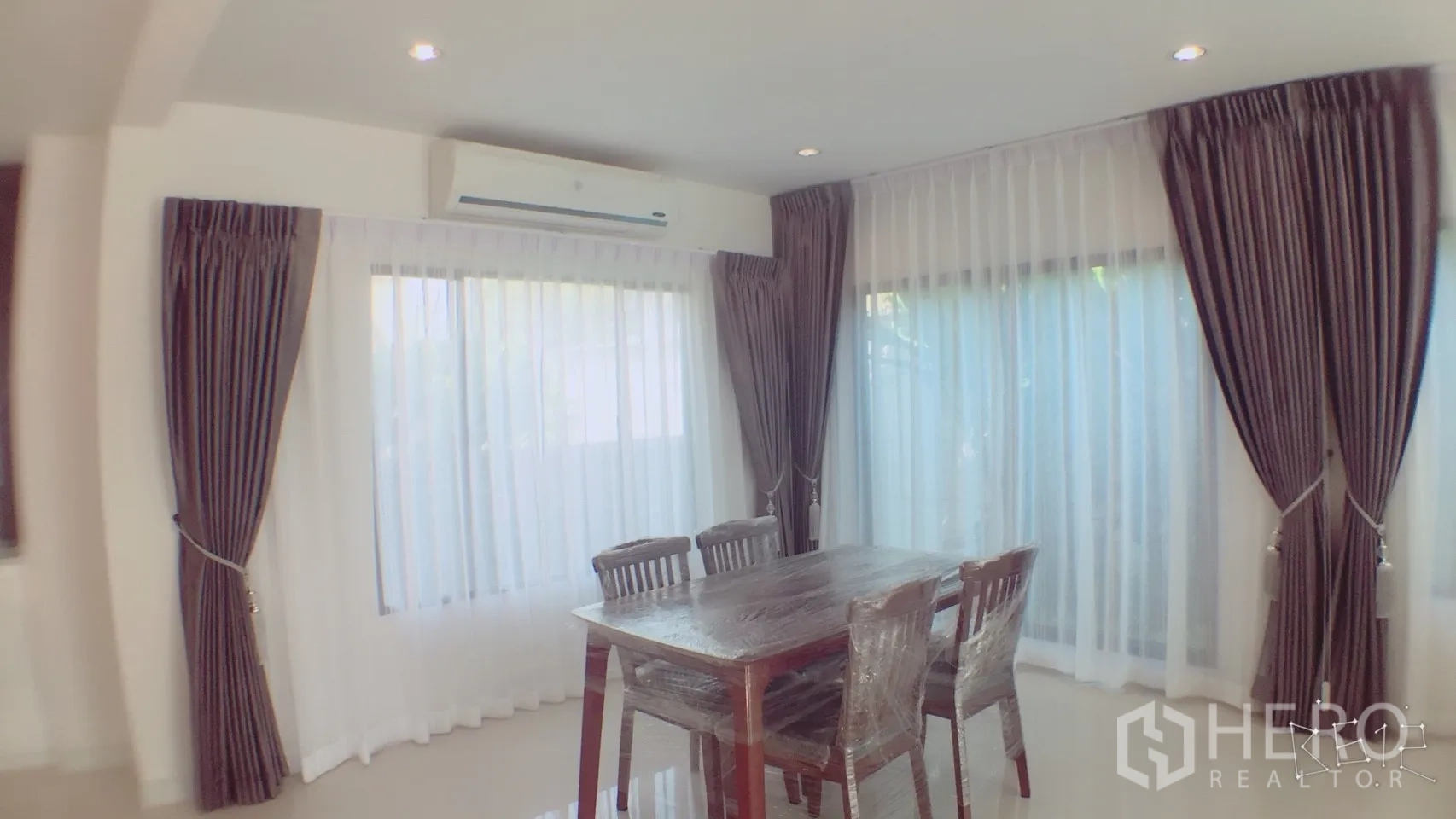 独立式住宅 出租在Suan Luang, Bangkok - 转角餐区，四人木餐桌，空调，大幅落地窗与窗帘。